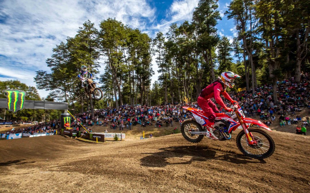 Motociclista realizando un salto en una carrera de enduro bajo el sol del atardecer, montañas de fondo